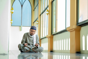 Fototapeta na wymiar Ramadan, Quran, Islam, An Asian Muslim man is sitting and reading the Quran. The peace in the mosque makes it an energetic atmosphere of faith, with copy space.