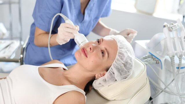 Young woman undergoing hardware facial treatment using cold hammer helping to shrink pores, repair damaged skin and relieve inflammation in modern cosmetology clinic