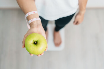 woman on weight scale and hand hold green Apple, choose fruit is Healthy food. Dieting control,...