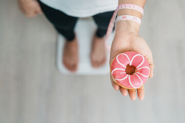 woman on weight scale and hand hold pink Donut, choose stop eating sweet is Unhealthy ealthy food....