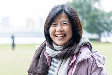 A smiling Taiwanese old woman spending winter in a large park along the river in Taipei, Taiwan 台湾台北市の川沿いの大きな公園で冬に過ごす笑顔の台湾人の老人女性