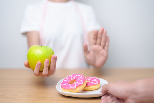 woman hand hold green Apple and reject donut, female fitness choose between fruit is Healthy and sweet is Unhealthy junk food. Dieting control, Weight loss, Obesity, eating lifestyle and nutrition