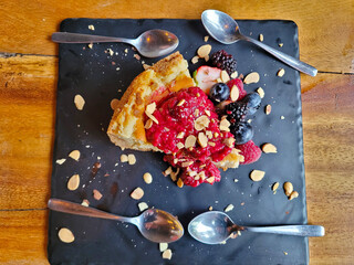 Delectable slice of cheesecake topped with fresh berries and almond flakes, served on a slate board for a rustic appeal, Vertical