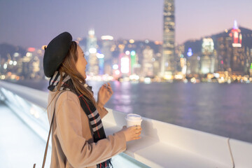A young Chinese woman in her 20s in a mini skirt looking at a group of skyscrapers on a deck by the sea on Hong Kong Island 香港島の海沿いのデッキで高層ビル群を眺めるミニスカートの20代の若い中国人女性