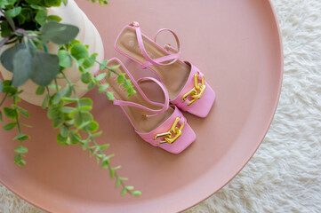Pink heeled sandals lie on a pink table and beige rug. Stylish summer women shoes. Trendy beauty female fashion top view