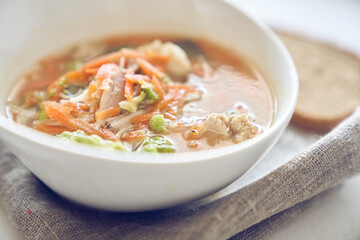 Side view of a healthy and delicious soup of vegetables and meat in a white plate on the table with bread with copy space. Soup with broccoli, carrots, meat, served with bread. Selective focus