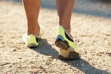 Person, runner and athlete with shoes for running, marathon or sports on dirt road or terrain. Closeup of athletic feet, footwear or getting ready for cardio, training or outdoor exercise and workout