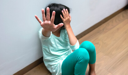 Unhappy depressed asian child sitting on floor at home. Holding out hand indicates resistance. Concept for campaign against child violence, abuse, pain, and bullying. 