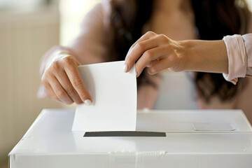 Fototapeta na wymiar Hand of a lady inserting a voting ballot into a slot of a white box