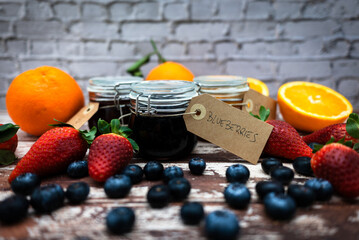 Homemade blueberry jam in glass jar with name tag. Glass jars with different types of jam on wooden table. Homemade orange, strawberry and blueberry jam