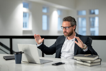 Obraz premium Business worker with laptop at office. Employee remote working in modern office. Business man on online meeting. Hispanic business man working online. Mature business man using laptop at workplace.