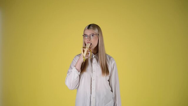 Gorgeous European girl eating a banana isolated on yellow background, studio