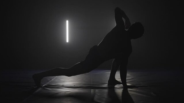 male athlete doing yoga stretches as workout warming up in black and white studio, silhouette yoga