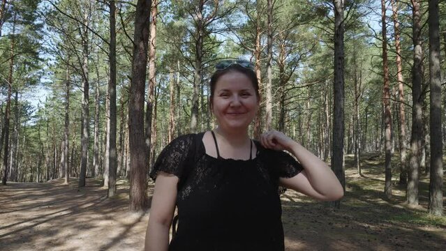 A white woman in her thirties beams at the camera amidst the serene woods of Stilo, Poland, exuding joy and tranquility in the heart of nature