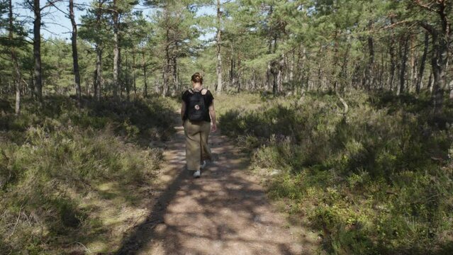 white woman in her thirties wanders along a forest path in Stilo, Poland, her back turned to the camera, lost in the tranquil beauty of nature.