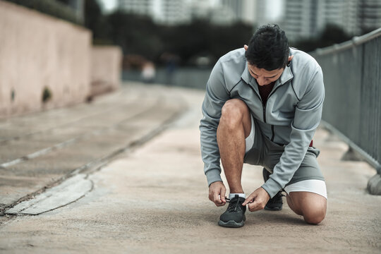 A man tying shoelaces on sport shoes in the city center park before cardio workout, running. Health and Lifestyle in big city life concept.
