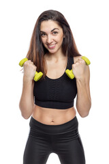 A slender woman in sportswear with green dumbbells does exercises. Beautiful smiling brunette in a black top and leggings. Activity and healthy lifestyle. Isolated on a white background. Vertical.