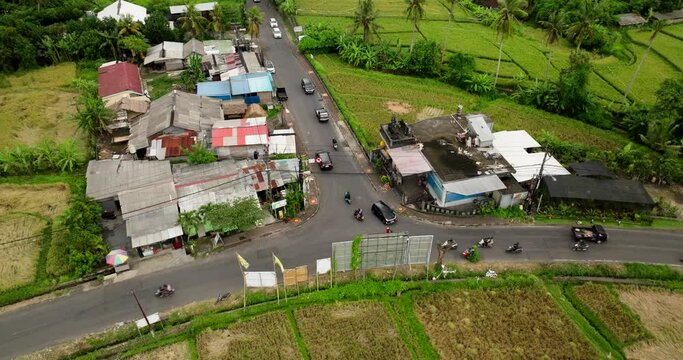 Motorcycle and car traffic at T-junction of countryside road in Bali. Aerial