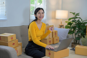 Young Asian woman startup small business freelance sitting on the sofa, packaging her product for her customer.