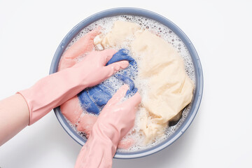 Female hands in rubber gloves washing clothes in basin on white background, top view.