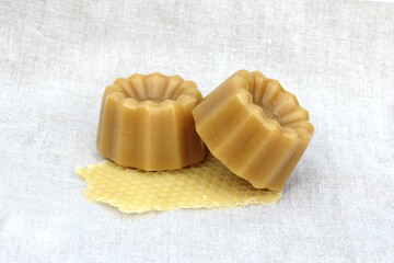Shaped pieces of natural bee wax piled up with honey comb fragment on a linen background