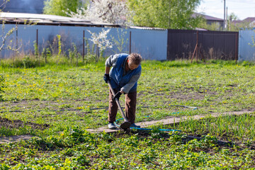 A woman works with a hoe in the garden in the spring