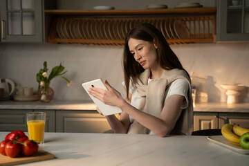 A young woman stands in her sunlit kitchen, smiling broadly as she engages in a casual video chat...