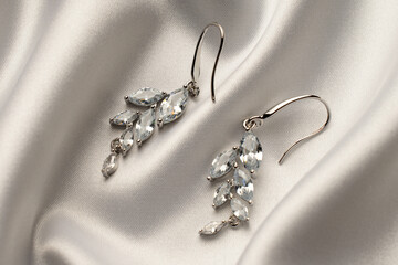 Silver earrings with diamonds on beige silk background