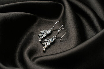 Jewelry. Silver earrings with diamonds on black silk background