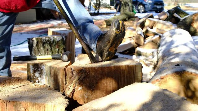 Slow motion of iron lever or rod being used to separate two halves of split oak stump or log while preparing firewood.