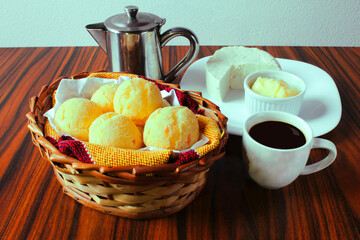 Brazilian cheese bread. Seletive focus. Basket of cheese bread with coffee, teapot, butter and white cheese. Brazilian breakfast.