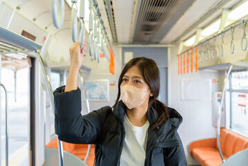 Asian woman passenger with face mask holding the handle in tram, train, bus or subway.