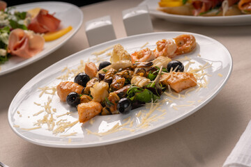 Salad with seafood, grilled salmon and black olives on a white plate