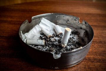 Burnt cigarettes in an ashtray on a wooden table with wet tissue inside