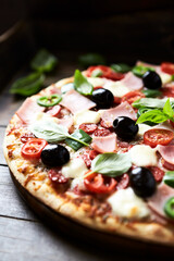 Pizza with ham, mozzarella cheese, cherry tomatoes, green and jalapeno pepper, black olives and fresh basil. Dark background. Close up.