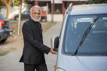 Senior man or businessman standing besides new car with keys.