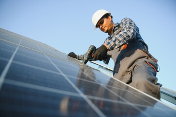 An Indian worker in uniform and with tools works on a solar panel farm