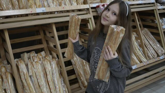 A teenage girl holds two baguettes in her hands, chooses and buys bread in the supermarket or bakery