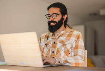 teleworking concept: Hispanic man wears headphones and uses laptop to join video meeting at home freely