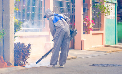 Healthcare worker using fogging machine to spraying insecticide in drainage ditch on the street in...