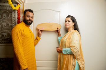 Happy indian couple holding the name plate of their new house. Buy property or Real estate concept....