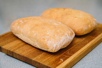 Freshly Baked Ciabatta Bread on Wooden Board. Two loaves of crusty ciabatta bread resting on a wooden cutting board, showcasing the art of traditional baking.
