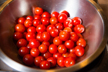 Bright Cherry Tomatoes in a Stainless Steel Bowl. Shiny, red cherry tomatoes fill a stainless steel bowl, washed and ready to be added to a variety of dishes.