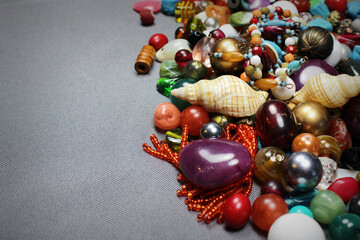 Composition of jewelry making supplies, colorful shiny mixed beads, pliers and craft wire on a gray fabric background, close up.