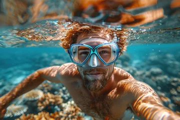 Schilderijen op glas Caucasian man in a mask swims on a coral reef © sofiko14