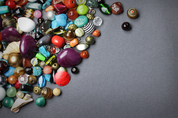 Composition of jewelry making supplies, colorful shiny mixed beads, pliers and craft wire on a gray fabric background, close up.