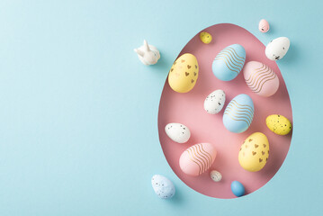 Greetings for Easter creativity theme. Top view shot featuring dyed eggs, showcased through a pink egg silhouette on a pastel blue surface, with a blank area for text or promo