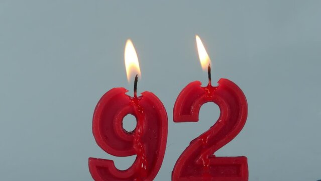 close up on timelapse melting a red number ninety two birthday candle on a white background.
