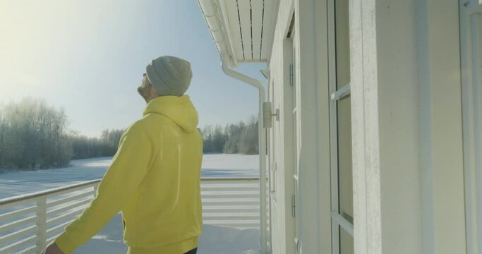 Young happy man enjoys first spring sun outside his forest home, side view