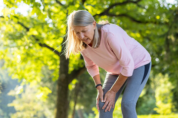 An elderly woman injured her leg while running and walking. Standing in the park, holding his knee,...